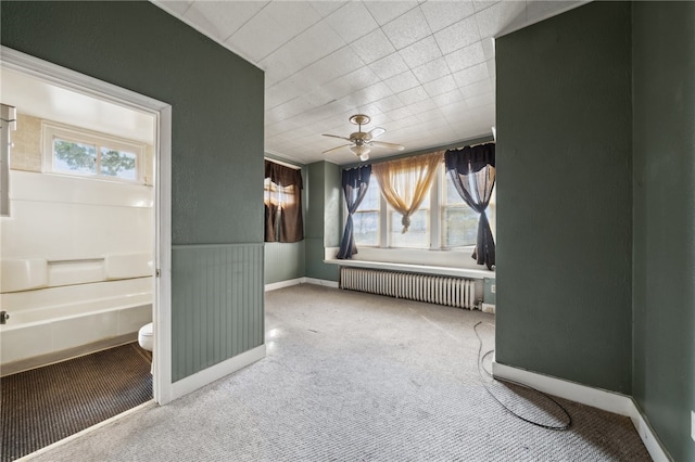 interior space featuring ceiling fan, toilet, and radiator heating unit