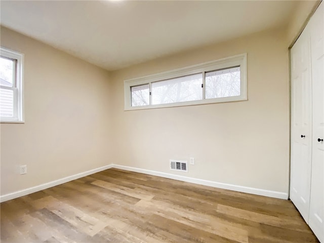 unfurnished bedroom featuring light wood-type flooring, a closet, and multiple windows