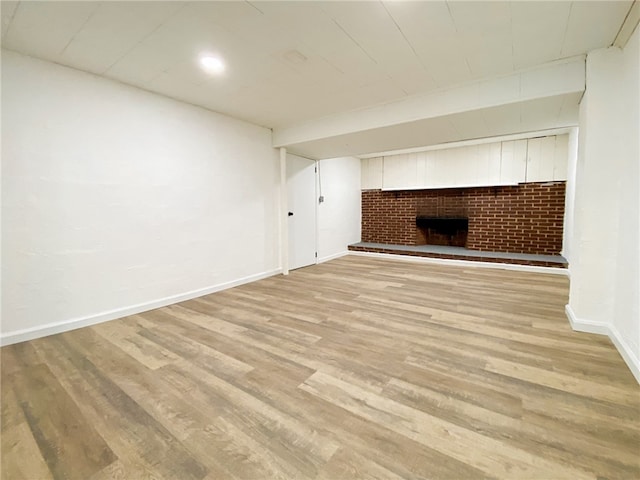 unfurnished living room featuring a fireplace, light hardwood / wood-style floors, and brick wall