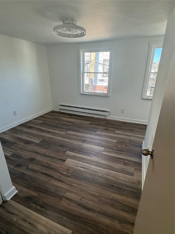 unfurnished room featuring dark hardwood / wood-style floors and a baseboard heating unit