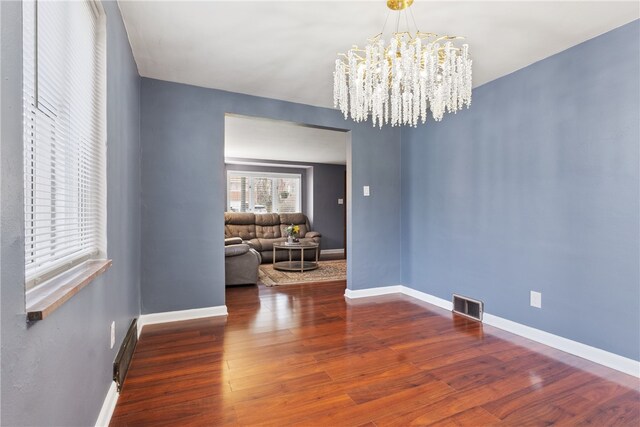 unfurnished dining area featuring a notable chandelier, wood finished floors, visible vents, and baseboards