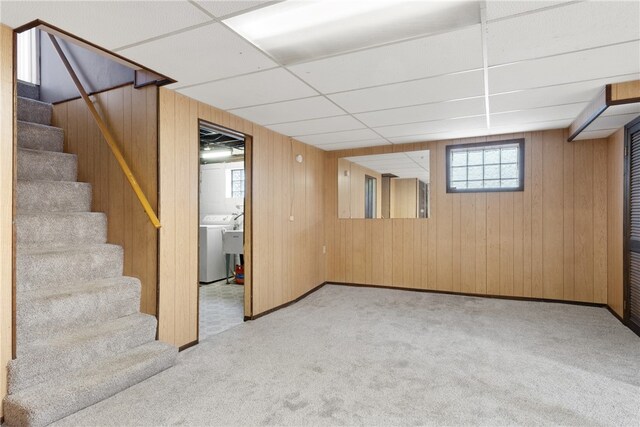 below grade area with a drop ceiling, wooden walls, carpet floors, stairs, and washer / dryer