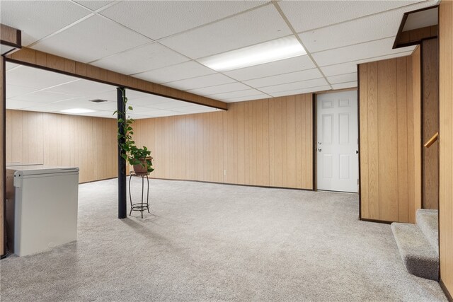 finished below grade area featuring wood walls, stairway, a drop ceiling, and refrigerator