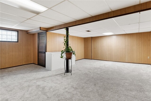 below grade area featuring carpet flooring, wooden walls, and a drop ceiling