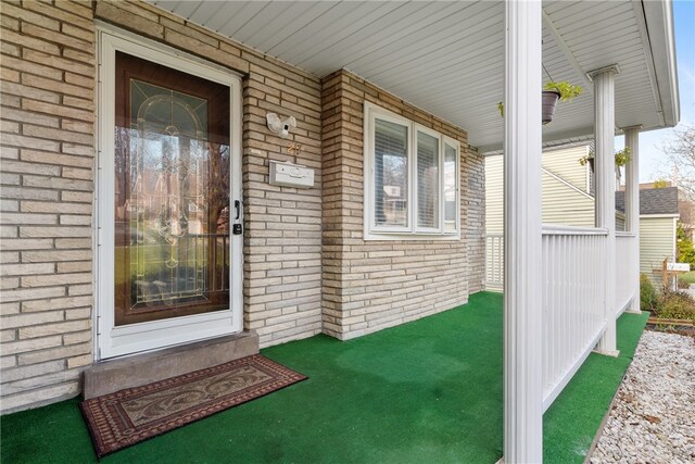 doorway to property featuring covered porch and brick siding