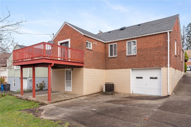 rear view of house with central AC, brick siding, driveway, roof with shingles, and a patio area