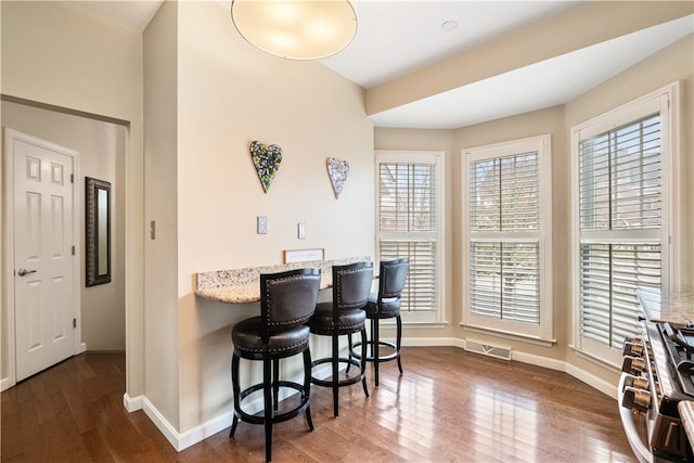 interior space with a kitchen breakfast bar, light stone countertops, and dark hardwood / wood-style floors