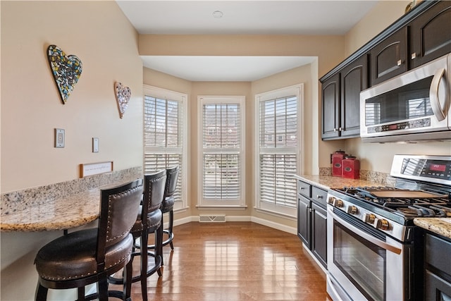 kitchen featuring hardwood / wood-style flooring, a wealth of natural light, light stone countertops, and appliances with stainless steel finishes