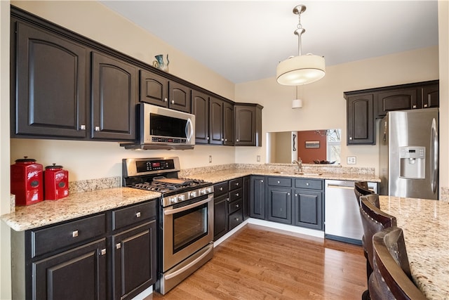 kitchen featuring pendant lighting, sink, light stone countertops, appliances with stainless steel finishes, and light hardwood / wood-style floors