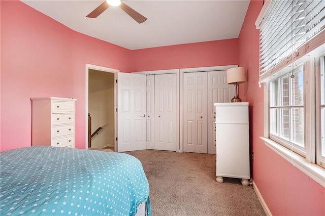 bedroom featuring ceiling fan, light colored carpet, and two closets