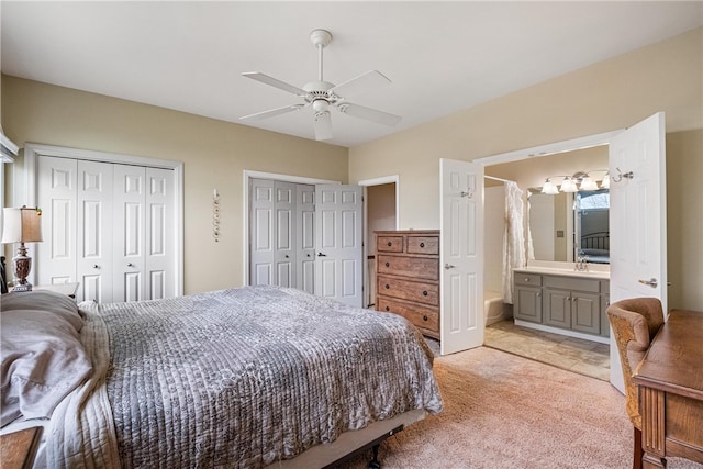 bedroom featuring ceiling fan, light colored carpet, multiple closets, and ensuite bath