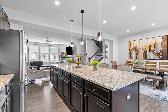 kitchen featuring stainless steel refrigerator, ceiling fan, a center island, hanging light fixtures, and dark wood-type flooring