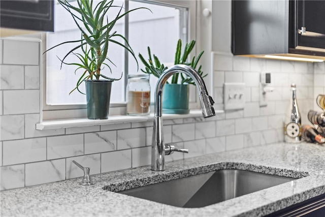 interior details with tasteful backsplash, light stone countertops, and sink