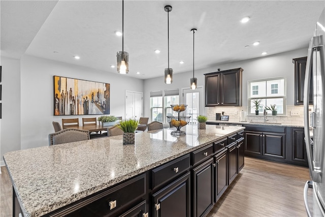 kitchen with sink, light stone counters, light hardwood / wood-style flooring, pendant lighting, and a kitchen island