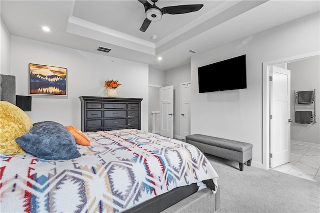 bedroom featuring a raised ceiling, connected bathroom, ceiling fan, and light carpet