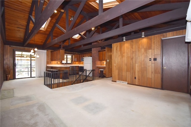 unfurnished living room with vaulted ceiling with beams, wood walls, and light colored carpet