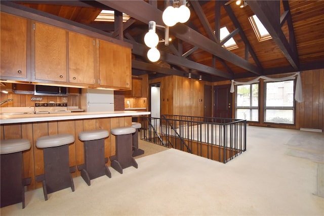 kitchen featuring wooden ceiling, light colored carpet, wood walls, and vaulted ceiling with skylight