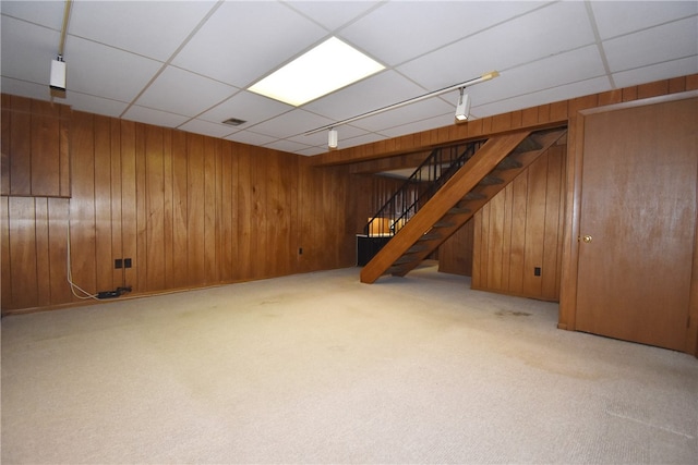 basement with a paneled ceiling, wood walls, and light carpet