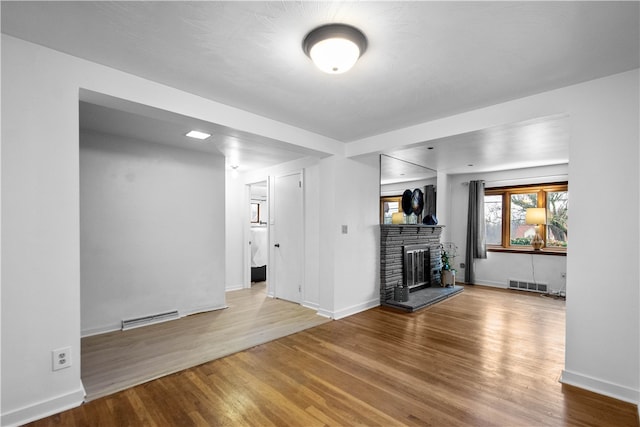 unfurnished living room with wood-type flooring and a stone fireplace