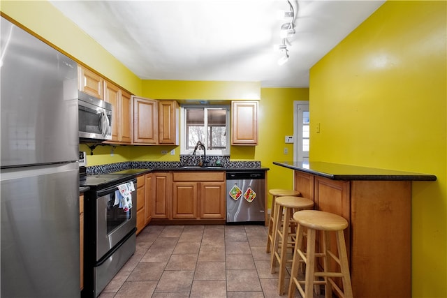 kitchen with track lighting, sink, light tile patterned floors, appliances with stainless steel finishes, and a breakfast bar area