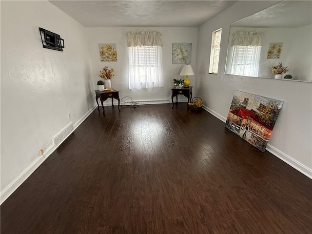 unfurnished room with dark hardwood / wood-style flooring and a baseboard heating unit