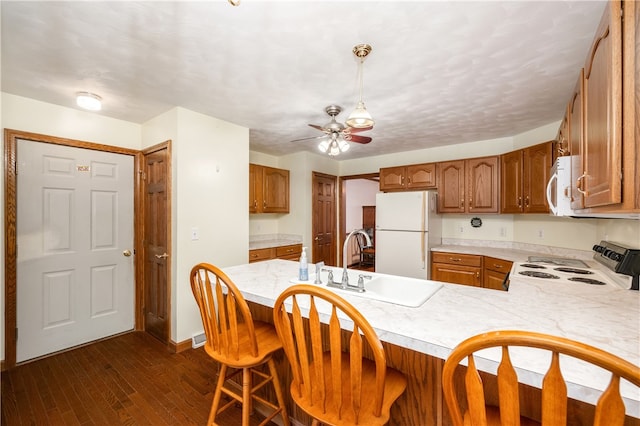 kitchen with white appliances, a kitchen breakfast bar, sink, dark hardwood / wood-style flooring, and kitchen peninsula