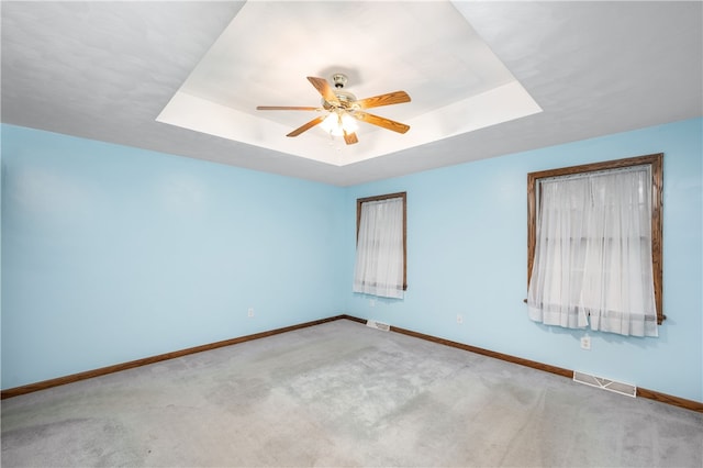 carpeted empty room with ceiling fan and a raised ceiling