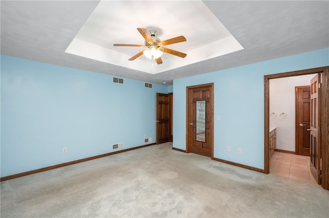 unfurnished bedroom with a raised ceiling, ceiling fan, light colored carpet, and ensuite bathroom