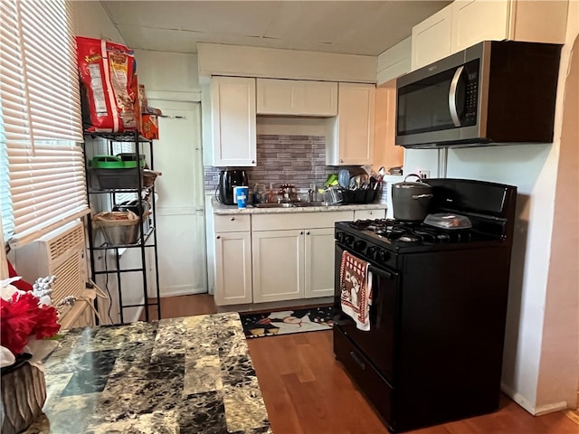 kitchen featuring light stone countertops, black range with gas stovetop, sink, wood-type flooring, and white cabinets