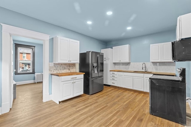 kitchen with stainless steel refrigerator with ice dispenser, light hardwood / wood-style floors, radiator heating unit, butcher block countertops, and white cabinetry