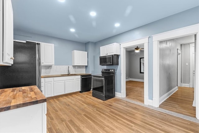 kitchen with white cabinets, black appliances, sink, light hardwood / wood-style flooring, and butcher block countertops