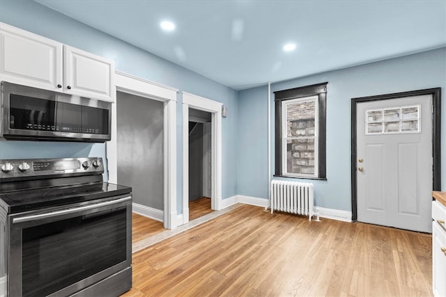 kitchen with radiator, white cabinetry, light hardwood / wood-style flooring, and stainless steel appliances