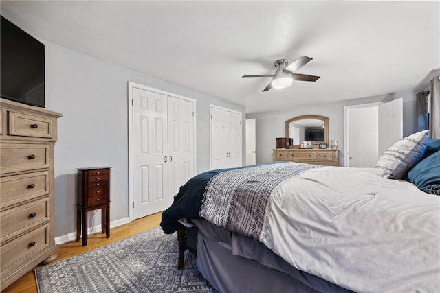 bedroom with ceiling fan, light hardwood / wood-style floors, and two closets