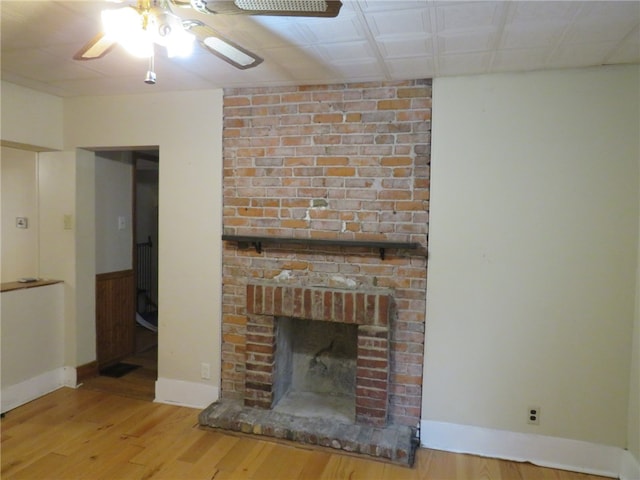 unfurnished living room with ceiling fan, wood-type flooring, and a brick fireplace