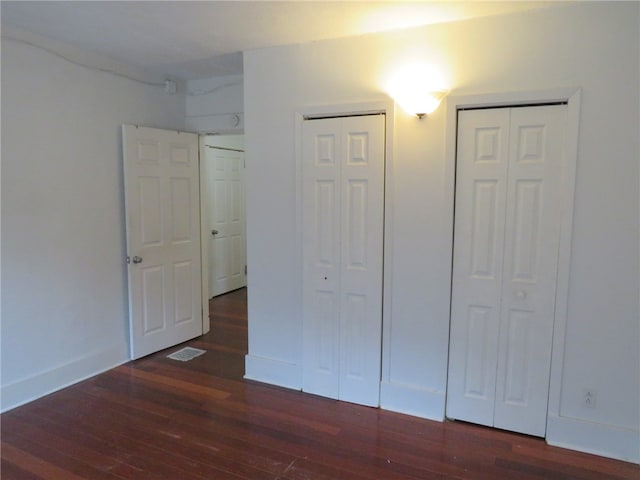 unfurnished bedroom with dark hardwood / wood-style flooring and multiple closets