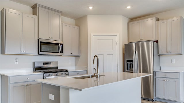 kitchen with stainless steel appliances, a kitchen island with sink, gray cabinetry, and sink