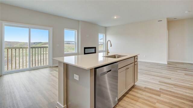 kitchen with light wood-type flooring, stainless steel dishwasher, sink, a center island with sink, and white cabinets