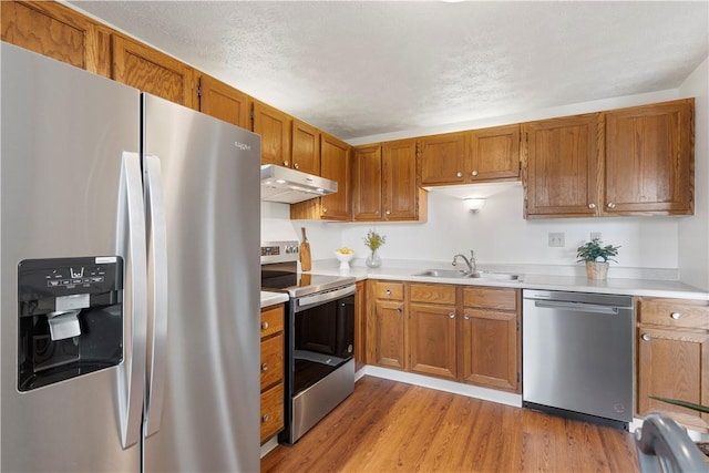 kitchen featuring sink, stainless steel appliances, light wood-type flooring, and a textured ceiling