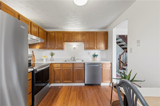 kitchen featuring sink, stainless steel appliances, light wood-type flooring, and a textured ceiling