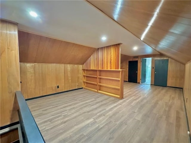 additional living space featuring wood walls, lofted ceiling, and light hardwood / wood-style flooring