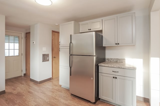 kitchen with light hardwood / wood-style floors, light stone countertops, and stainless steel refrigerator