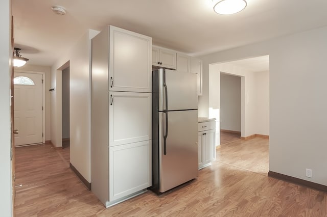 kitchen featuring stainless steel fridge, light hardwood / wood-style flooring, white cabinets, and light stone countertops