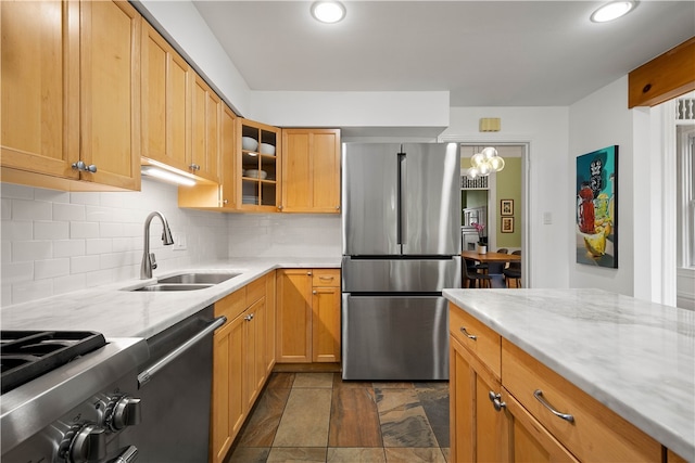 kitchen with light stone countertops, sink, stainless steel appliances, tasteful backsplash, and decorative light fixtures