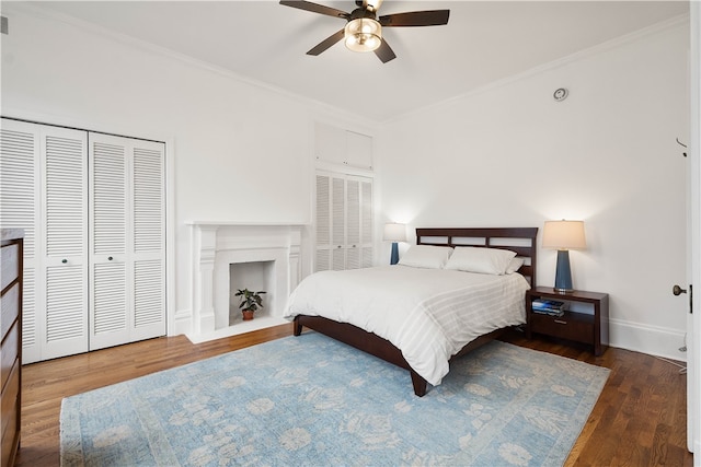 bedroom featuring two closets, crown molding, ceiling fan, and dark wood-type flooring