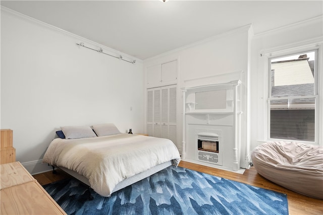 bedroom with heating unit, wood-type flooring, ornamental molding, and a closet