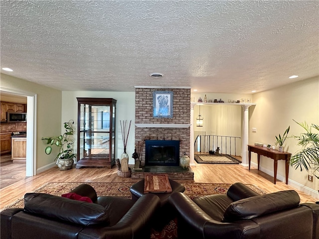 living room featuring ornate columns, light wood-type flooring, a textured ceiling, and a brick fireplace