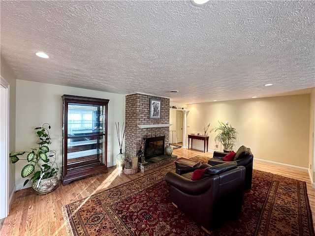 living room featuring wood-type flooring, a textured ceiling, and a brick fireplace