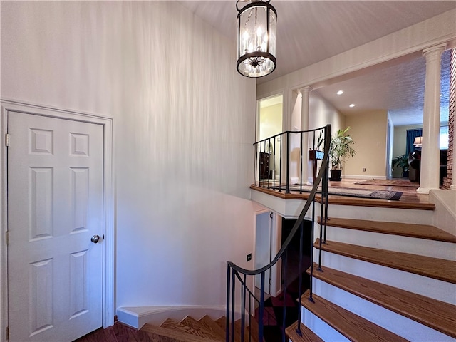 stairway with ornate columns, hardwood / wood-style flooring, and an inviting chandelier