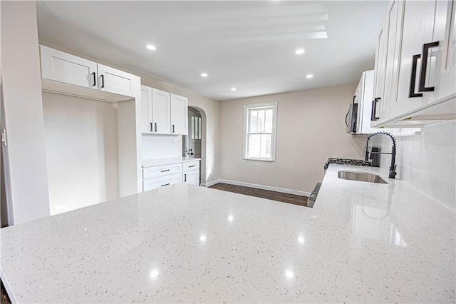 kitchen with kitchen peninsula, light stone countertops, sink, and white cabinets