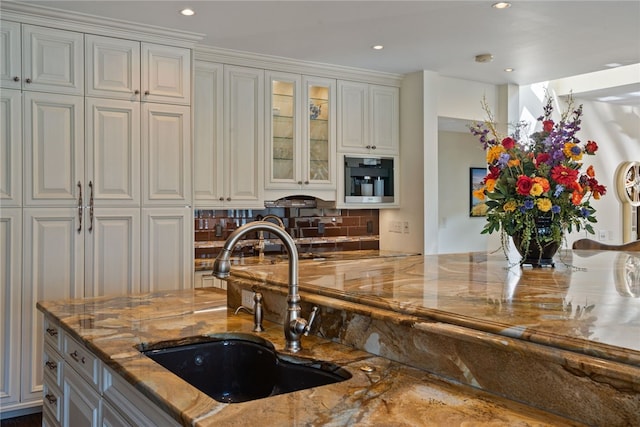 kitchen with backsplash, white cabinets, sink, ornamental molding, and stone countertops